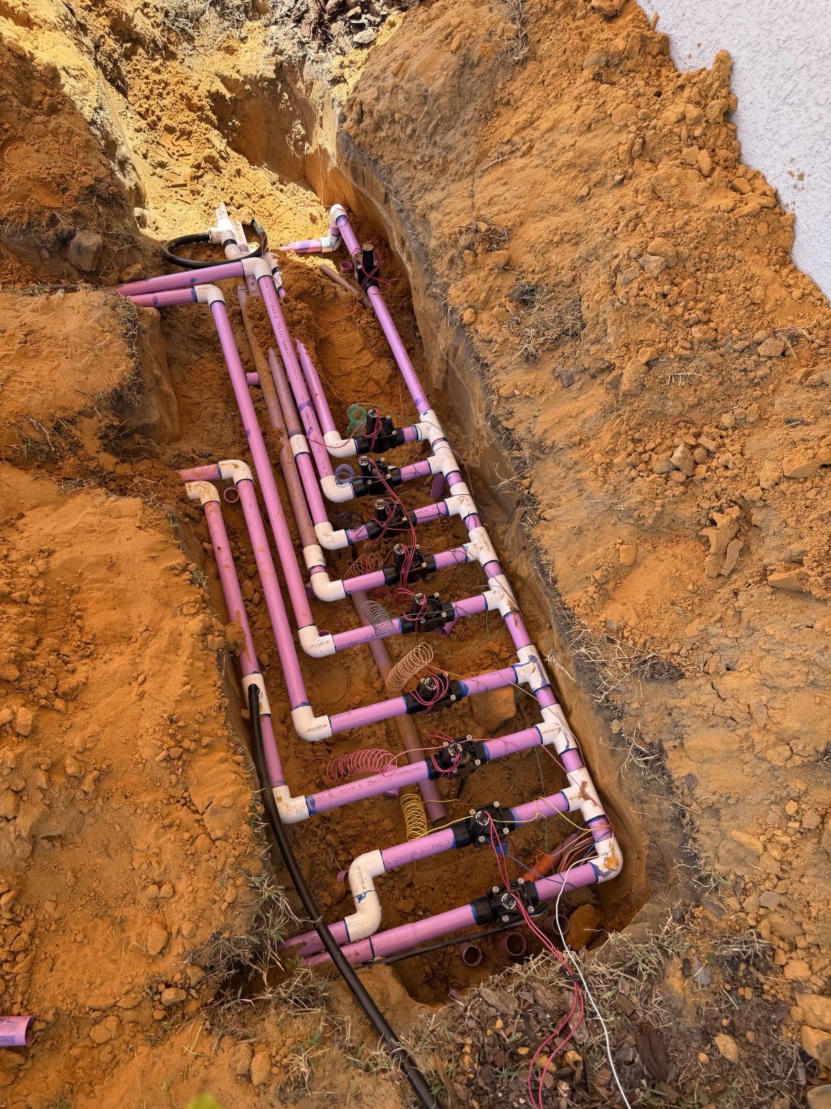 Ten-valve manifold plumbed in purple reclaimed-water PVC in an open trench
